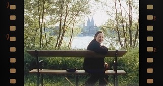 Film still: the actress as Maria Einsmann on a bench by the Rhine