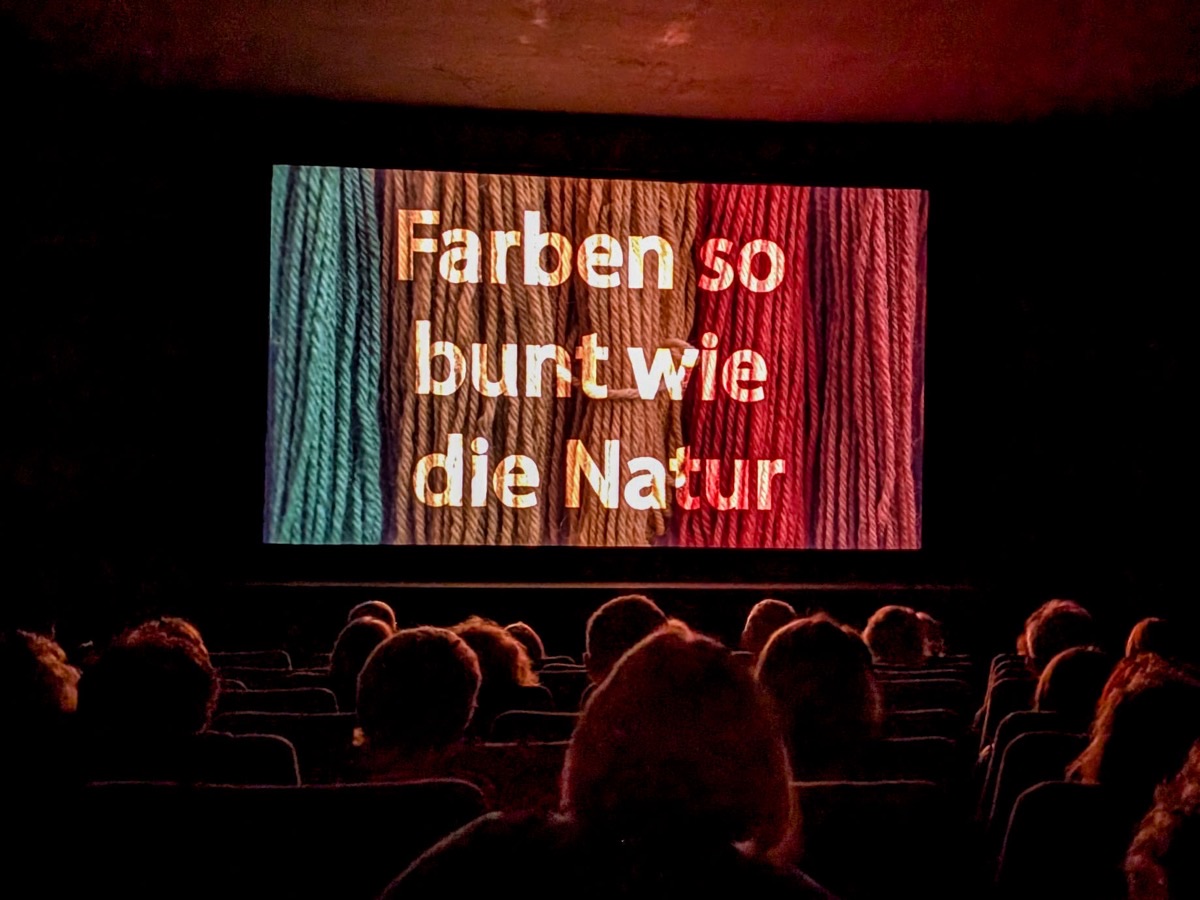 Publikum im Kinosaal vor der Leinwand mit dem Titel „Farben so bunt wie die Natur“